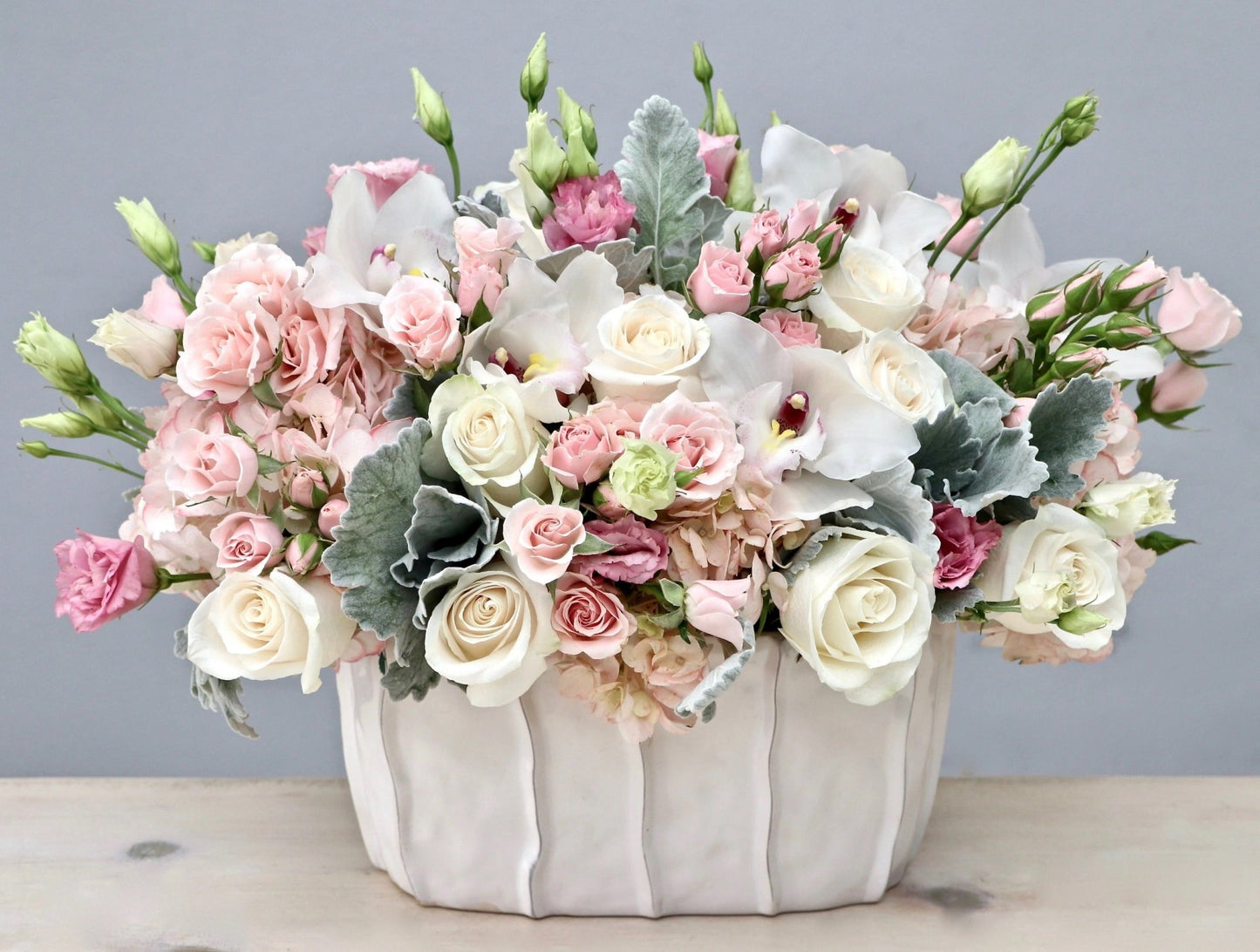 flower arrangement with orchids, lisianthus, pink spray roses, ivory roses and hydrangea in a white vase